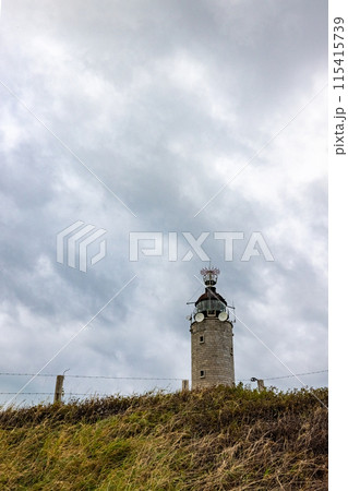 An Old Stone Lighthouse stands tall under a stormy sky, radiating heritage and maritime history An Old Stone Lighthouse stands tall under a stormy sky, radiating heritage and maritime history 115415739