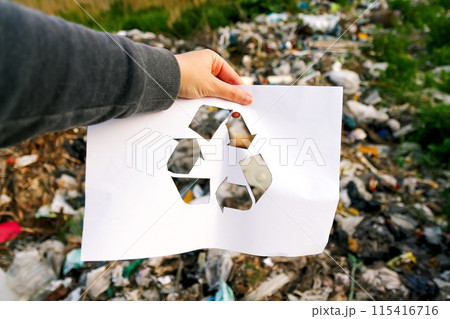 Hand holding a recycle logo against a garbage dump background. Suitable for environmental awareness campaigns 115416716