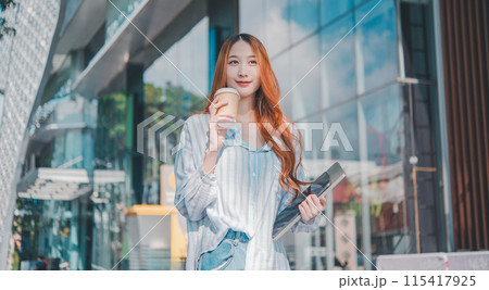 A woman with red hair is holding a cup of coffee and a laptop 115417925