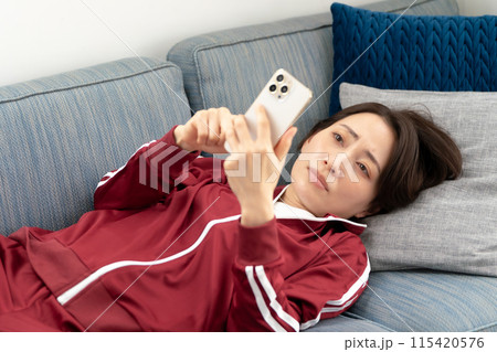 ソファーでスマホを見る女性　ストレス 115420576