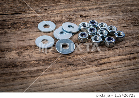 Stack of flat washer and zinc plated hexagon nuts on a dark wood texture background 115420725