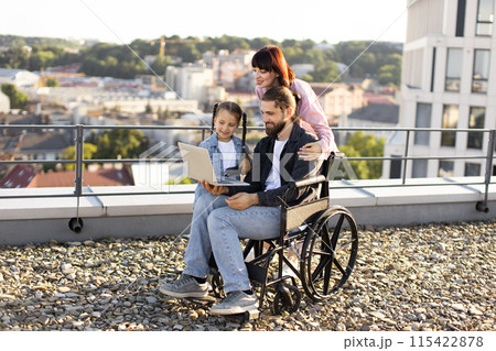 Happy family with man in wheelchair using laptop outdoors Happy family with man in wheelchair using laptop outdoors 115422878