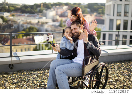 Happy family taking a selfie outdoors with wheelchair user 115422927
