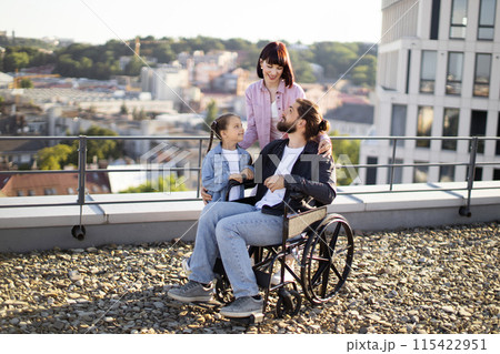 Young man in wheelchair having fun with family on terrace of house. 115422951