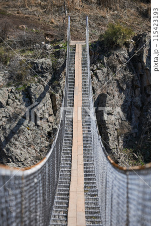 Suspension excursion bridge over the gorge. Sightseeing holiday tour in Kyrgyzstan. Crossing between two mountains 115423193