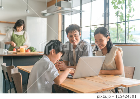 ダイニングでパソコンを見る親子とキッチンで料理する母親 115424501