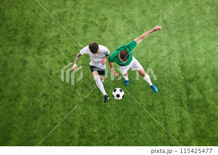 Aerial view. Two male soccer players compete for possession of ball on green lush playground. Aerial view. Two male soccer players compete for possession of ball on green lush playground. 115425477