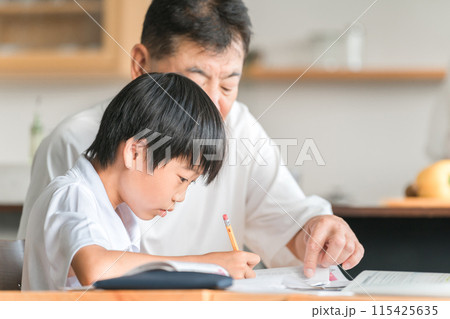 家のダイニングで孫の宿題を教える高齢者男性と小学生の子供 115425635