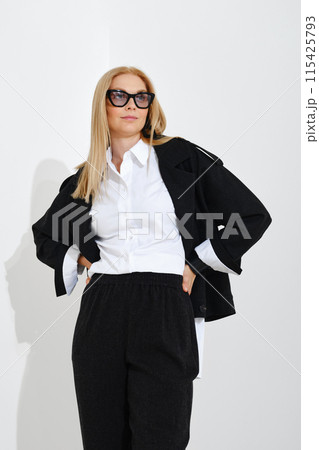 Modern woman in a classic suit holding her hands on her waist and looking into the distance 115425793