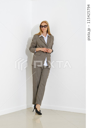 Stylish professional woman in checkered suit leaning against white wall 115425794