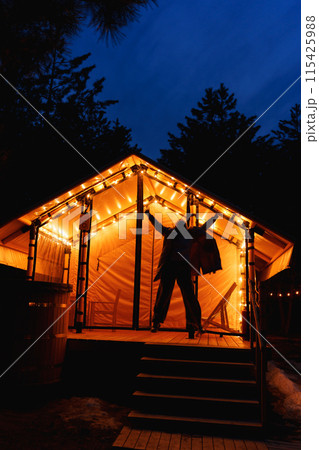 Glamping from tent houses in the forest in the dark. silhouette of a woman Glamping from tent houses in the forest in the dark. silhouette of a woman 115425988