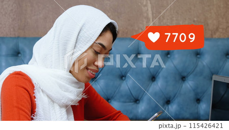 Digital composite of biracial woman with hijab typing on her phone while sitting on a lounge table Digital composite of biracial woman with hijab typing on her phone while sitting on a lounge table 115426421