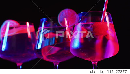 Glasses filled with vibrant drinks glow under neon lights 115427277