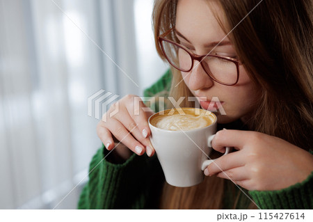 A woman with eyeglasses is sipping coffee from a cup A woman with eyeglasses is sipping coffee from a cup 115427614