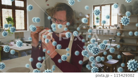 Image of covid 19 cells over man working in pottery studio wearing face mask 115429302