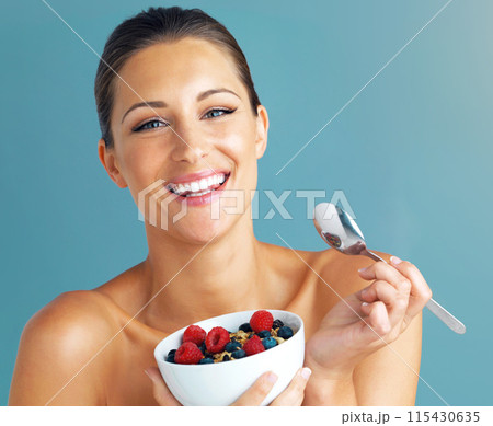 Woman, portrait and happy with cereal in studio for healthy meal, nutrition diet and digestion benefits. Smile, breakfast and female fitness model, isolated on blue background and eating food in bowl 115430635