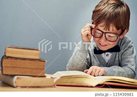 Boy, books and reading in studio with space for mockup, glasses and thinking for learning by blue background. Child, textbook and education with smile, study or scholarship for development at academy 115430981