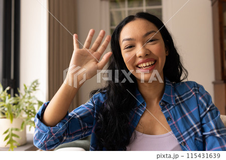 Young biracial woman waves at the camera from home on video call 115431639