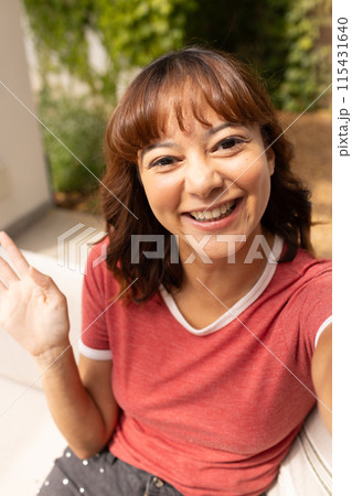 Young biracial woman waves cheerfully on video call 115431640