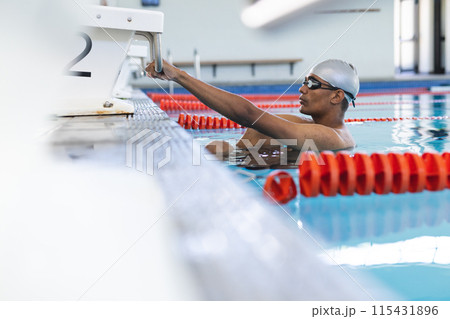 Young biracial male athlete swimmer prepares for a swim at an indoor pool Young biracial male athlete swimmer prepares for a swim at an indoor pool 115431896