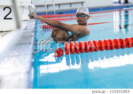 Young biracial male athlete swimmer prepares for a swim at an indoor pool Young biracial male athlete swimmer prepares for a swim at an indoor pool 115431903