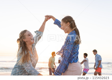 Two young Caucasian women dance on the beach at sunset 115432023