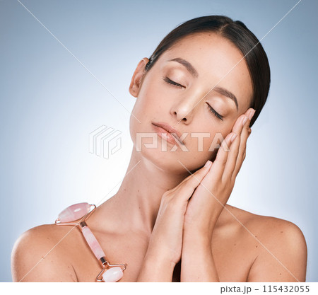 Face roller, woman and skincare for beauty in studio backdrop, satisfied with results in blue background. Female person, face and eyes closed with cosmetic product for glow, dermatology and wellness 115432055
