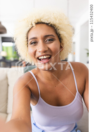 Young biracial woman with curly blonde hair smiles at the camera on a video call 115432400