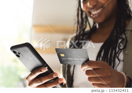 A young African American woman smiles while holding a credit card and a smartphone 115432451