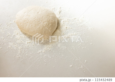A ball of dough sits atop a dusting of flour on a white surface with copy space 115432489