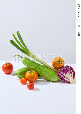 Fresh organic vegetables featured in center of white countertop against light gray background, including green squash, leek, tomato and purple cabbage. Photo for vegan culinary product promotion 115432632