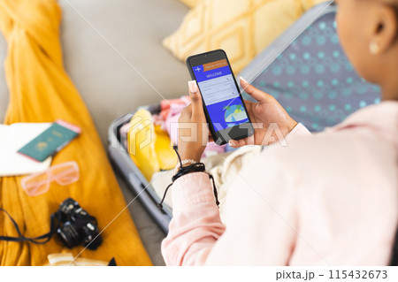 A young African American woman checks her phone, surrounded by travel essentials A young African American woman checks her phone, surrounded by travel essentials 115432673