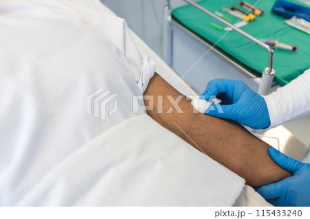 A healthcare professional is preparing a patient's arm for a procedure 115433240