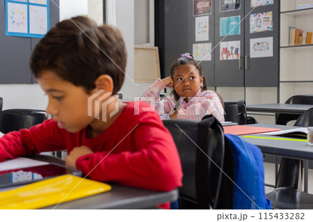 Biracial boy is focused on his work in a school classroom, while a biracial girl looks pensive 115433282
