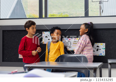 Biracial boy converses with an African American boy and biracial girl in a school classroom Biracial boy converses with an African American boy and biracial girl in a school classroom 115433295