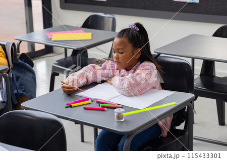 Biracial girl focused on drawing in a school classroom setting 115433301