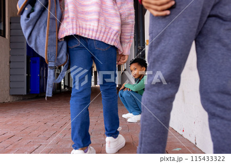 African American boy sits crouched between other children in school, looking sad 115433322