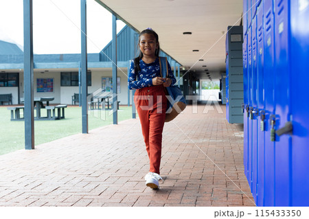 Biracial girl with a backpack stands by blue lockers at school Biracial girl with a backpack stands by blue lockers at school 115433350