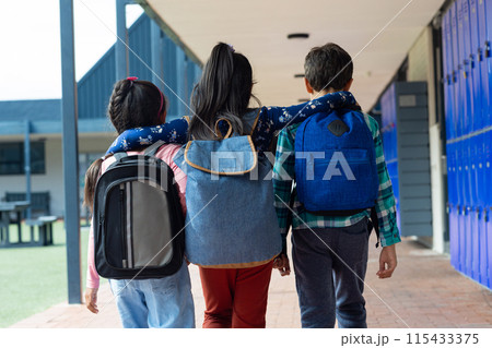 Three children are walking down a school corridor, arms around each other 115433375