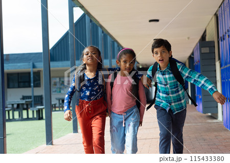 Three biracial children walk through a school corridor with lockers 115433380