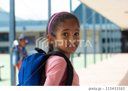 Biracial girl with a pink headband and a blue backpack smiles at school Biracial girl with a pink headband and a blue backpack smiles at school 115433383