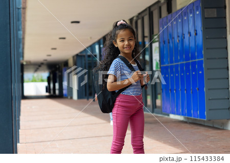 Biracial girl with a backpack stands smiling at school Biracial girl with a backpack stands smiling at school 115433384