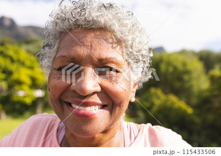 Senior biracial woman with curly gray hair smiles warmly outdoors 115433506