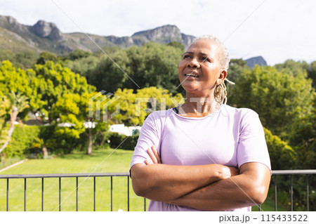 Senior biracial woman stands confidently outdoors, arms crossed, smiling, with copy space 115433522