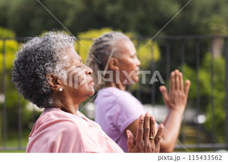 Senior African American woman and senior biracial woman practice yoga outdoors, both with grey hair Senior African American woman and senior biracial woman practice yoga outdoors, both with grey hair 115433562