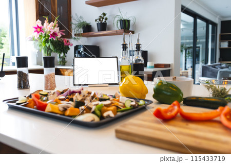 A tablet with a blank screen stands among various cooking ingredients on a kitchen counter 115433719
