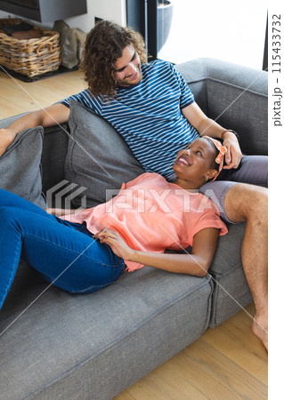 Diverse couple young African American woman and Caucasian man relax on a gray sofa, sharing a moment 115433732