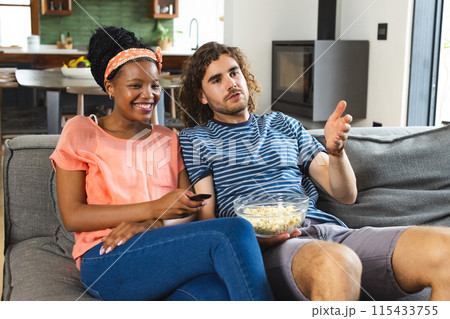 Diverse couple young African American woman and Caucasian man relax on a sofa, watching TV together Diverse couple young African American woman and Caucasian man relax on a sofa, watching TV together 115433755