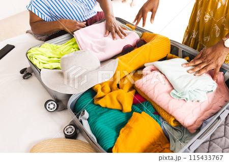 Senior African American woman and senior biracial woman pack a suitcase 115433767