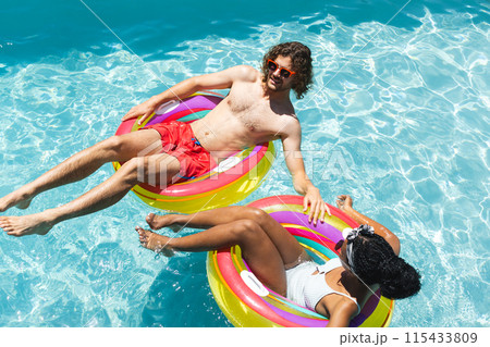 Caucasian man and African American woman relax on colorful pool floats Caucasian man and African American woman relax on colorful pool floats 115433809